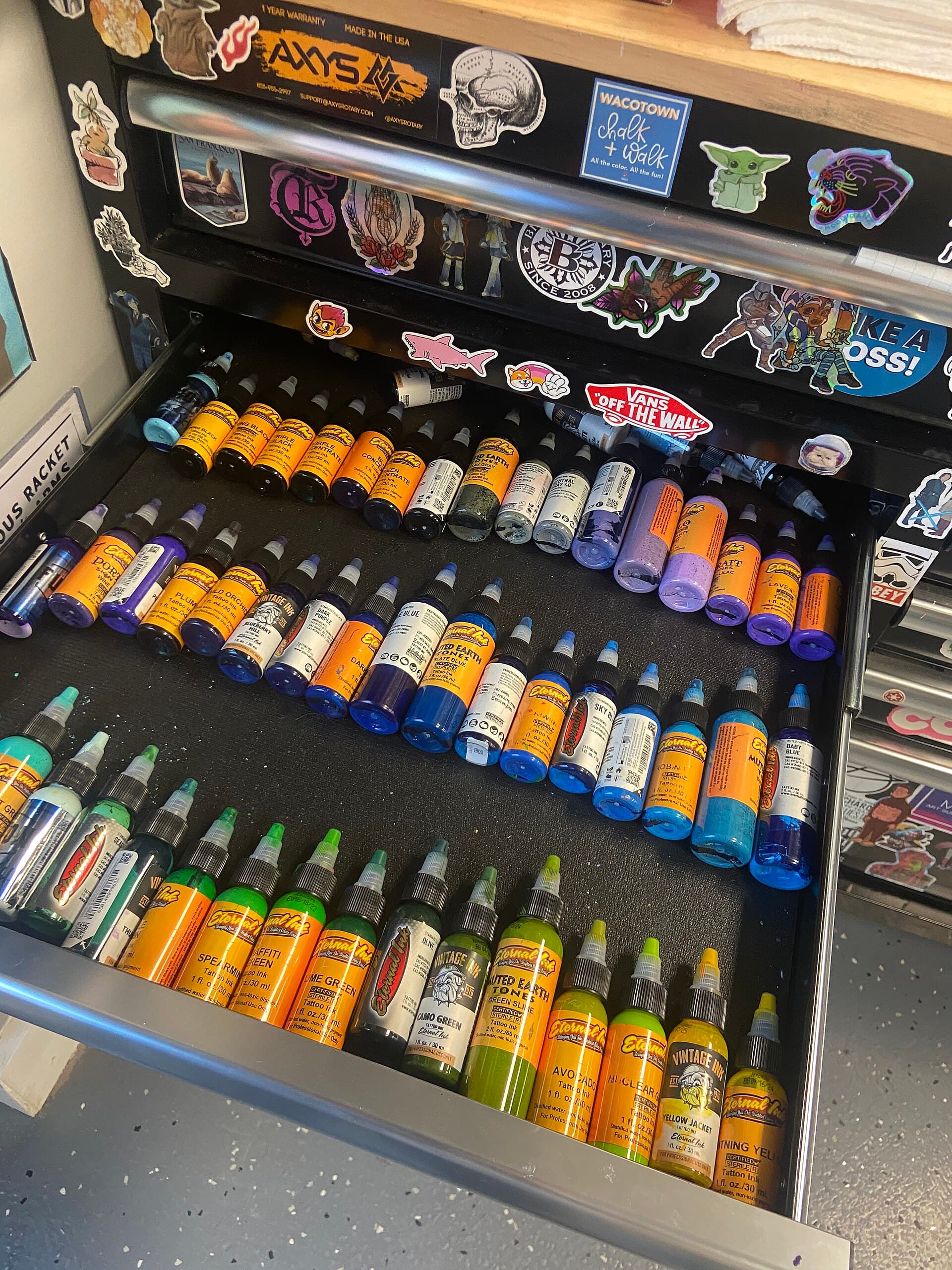 Cajón con frascos de tinta de tatuaje de colores ordenados en filas
